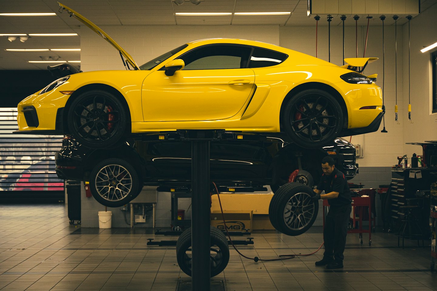 Technician working on a car wheel under a yellow sports car.